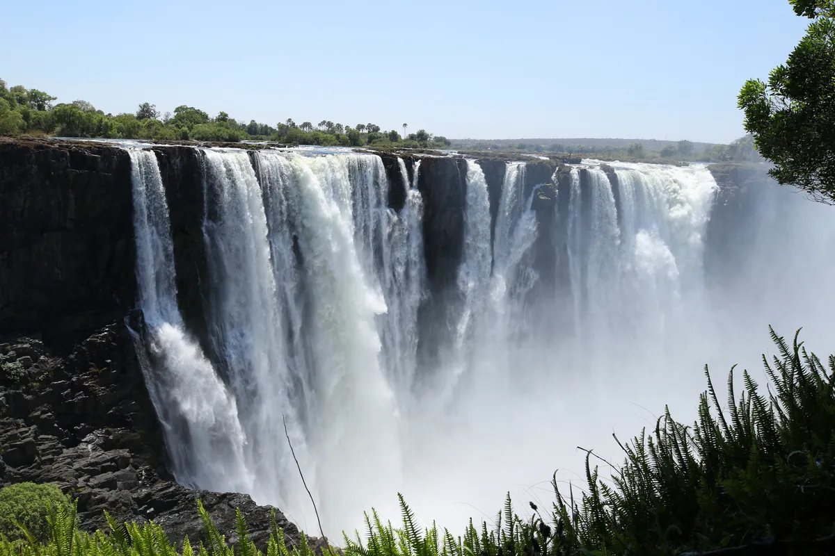 Victoria Falls pouring over a long basalt cliff into a gorge of mist