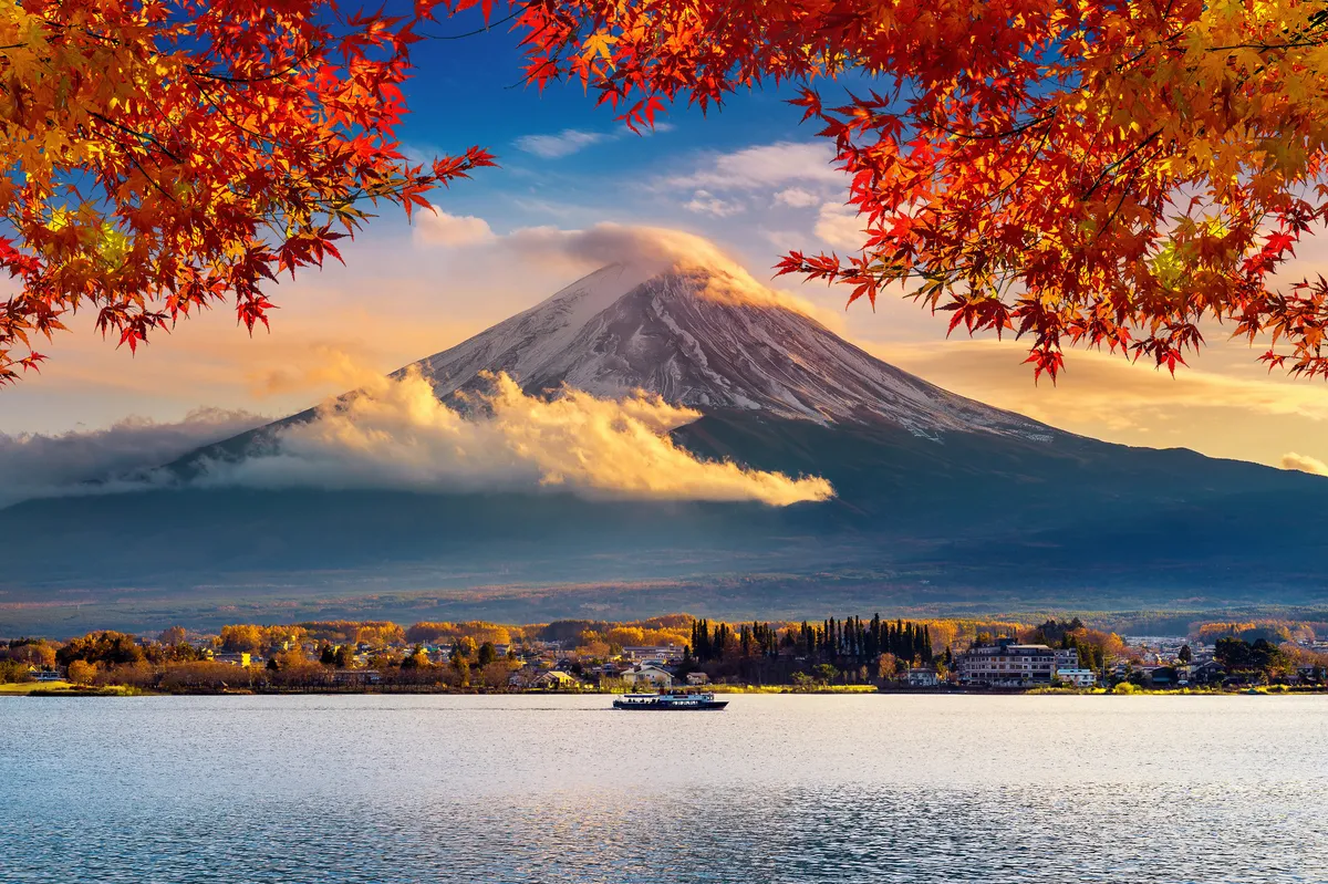 Snowcapped Mt. Fuji above a lake, framed by red autumn maple leaves