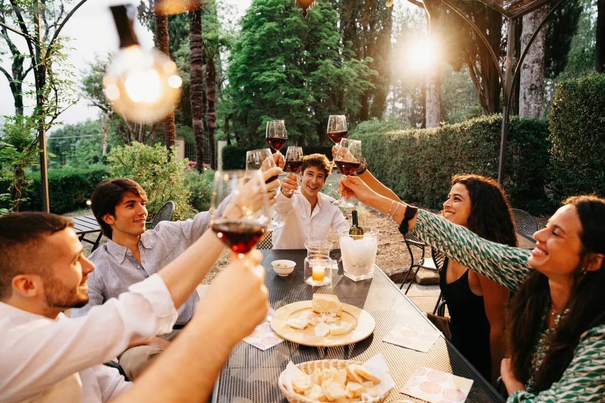 Friends raising glasses of red wine at an outdoor table in an Italian garden