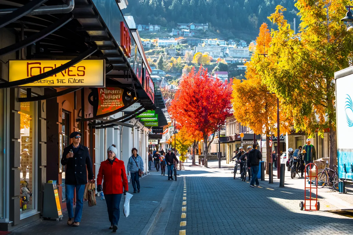 Shoppers on a Queenstown street lined with red and gold autumn trees